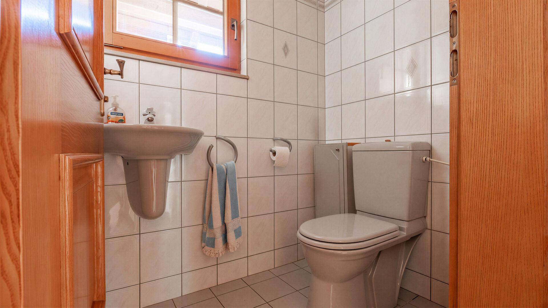 Kleines Badezimmer oder Gäste-WC mit Fliesen, Toilette und wandmontiertem Waschbecken.