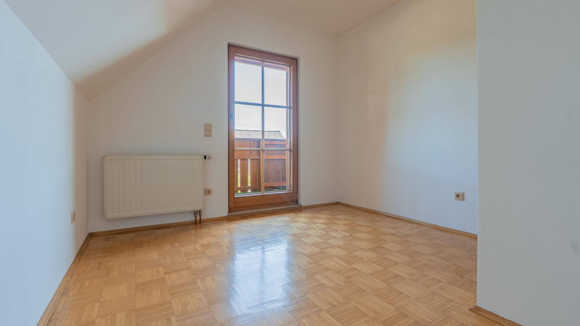 Geräumiges Schlafzimmer mit Parkettboden, Dachschräge und Zugang zu einem Balkon.