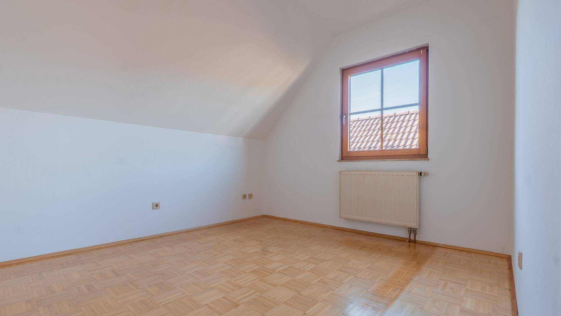 Helles Schlafzimmer mit Parkettboden, Dachschräge und Fenster, bereit zur individuellen Gestaltung.