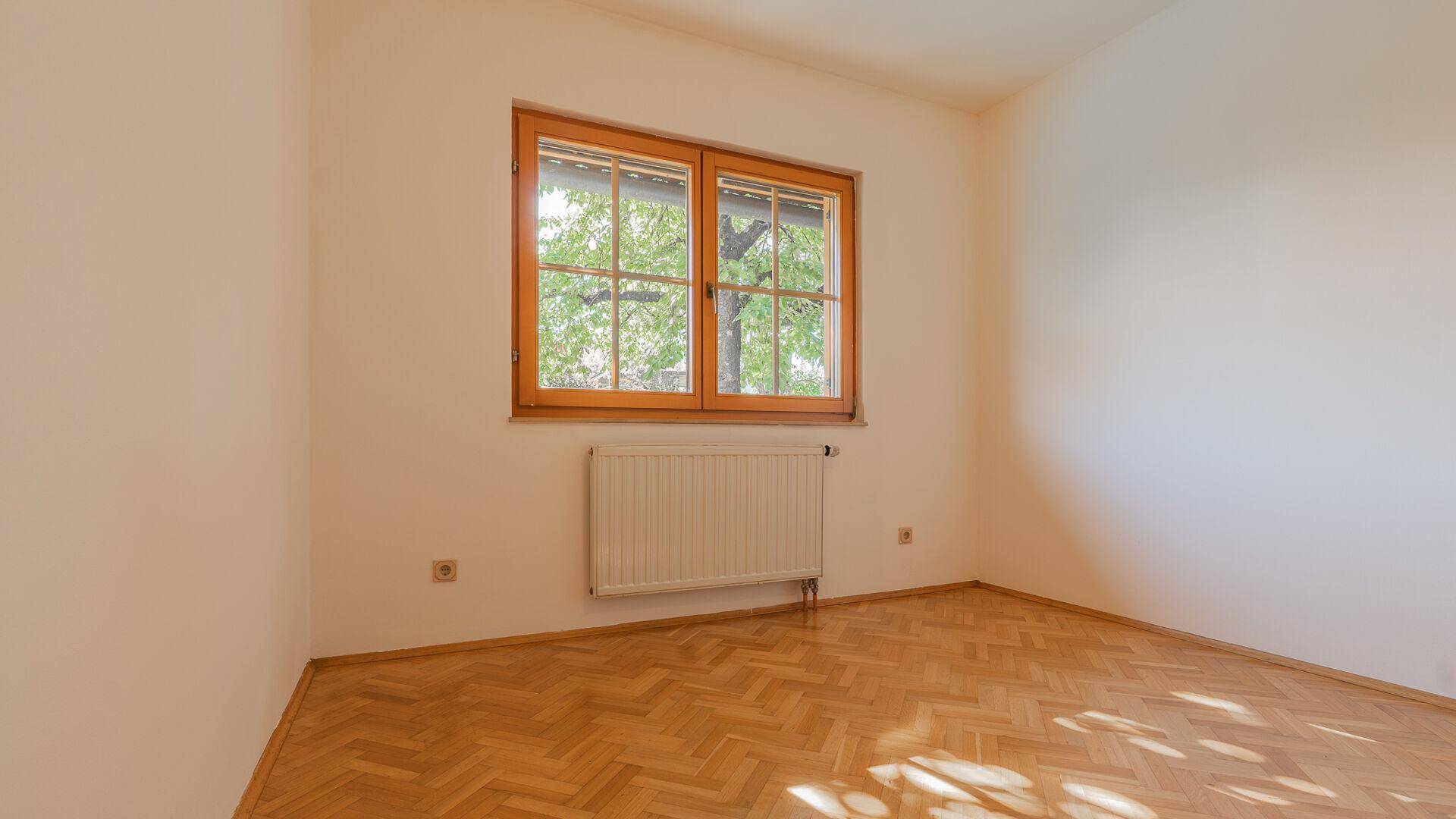 Helles Schlafzimmer mit Parkettboden, großem Fenster und Heizkörper, bereit zur Einrichtung.