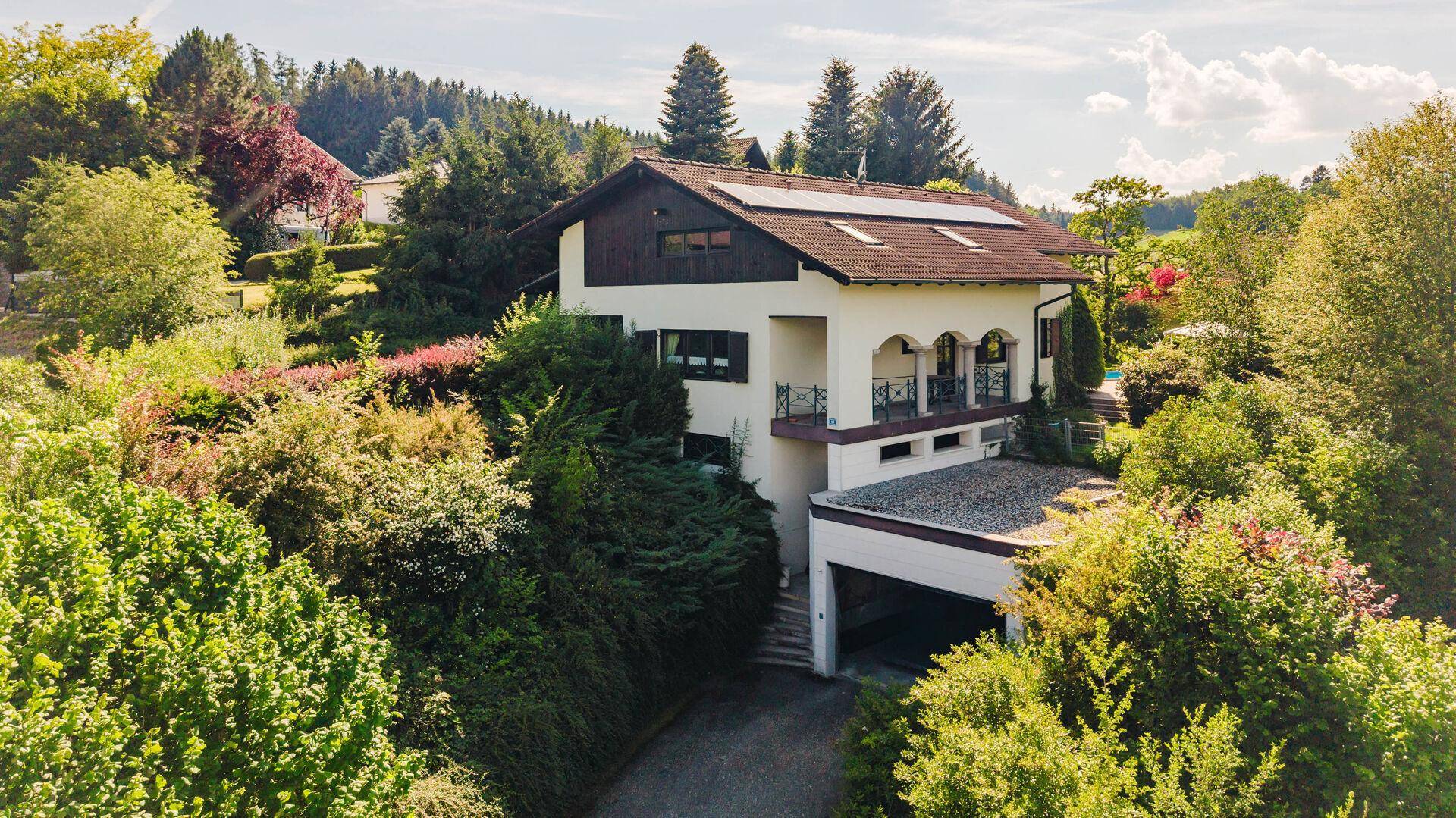 Ansicht des Hauses von vorne mit Balkonen, integrierter Garage und umgebender Naturlandschaft.