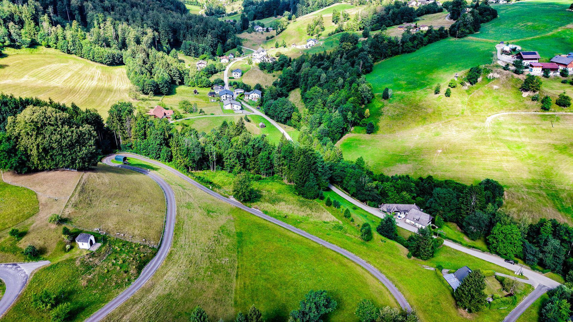 Weitläufige Luftaufnahme eines malerischen Tals mit verstreuten Häusern, Straßen und üppiger Natur.