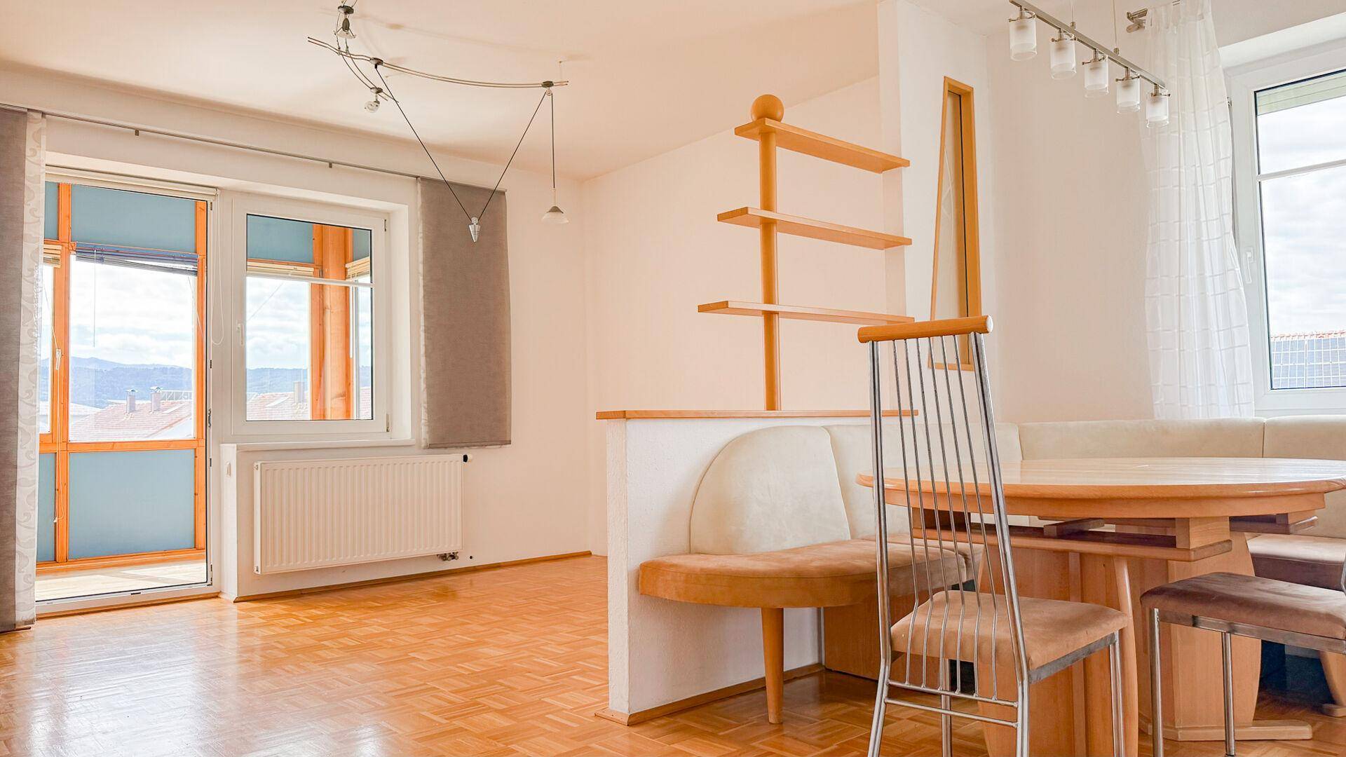 Heller Wohn- und Essbereich mit Parkettboden, Holzelementen und Zugang zum Balkon.