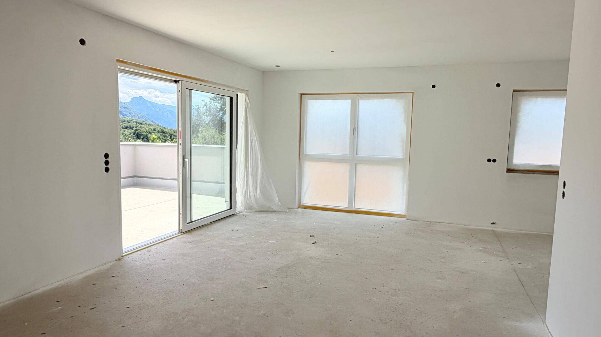 Heller Wohnraum im Rohbau mit Schiebetüren zum Balkon und Blick auf die Berge.