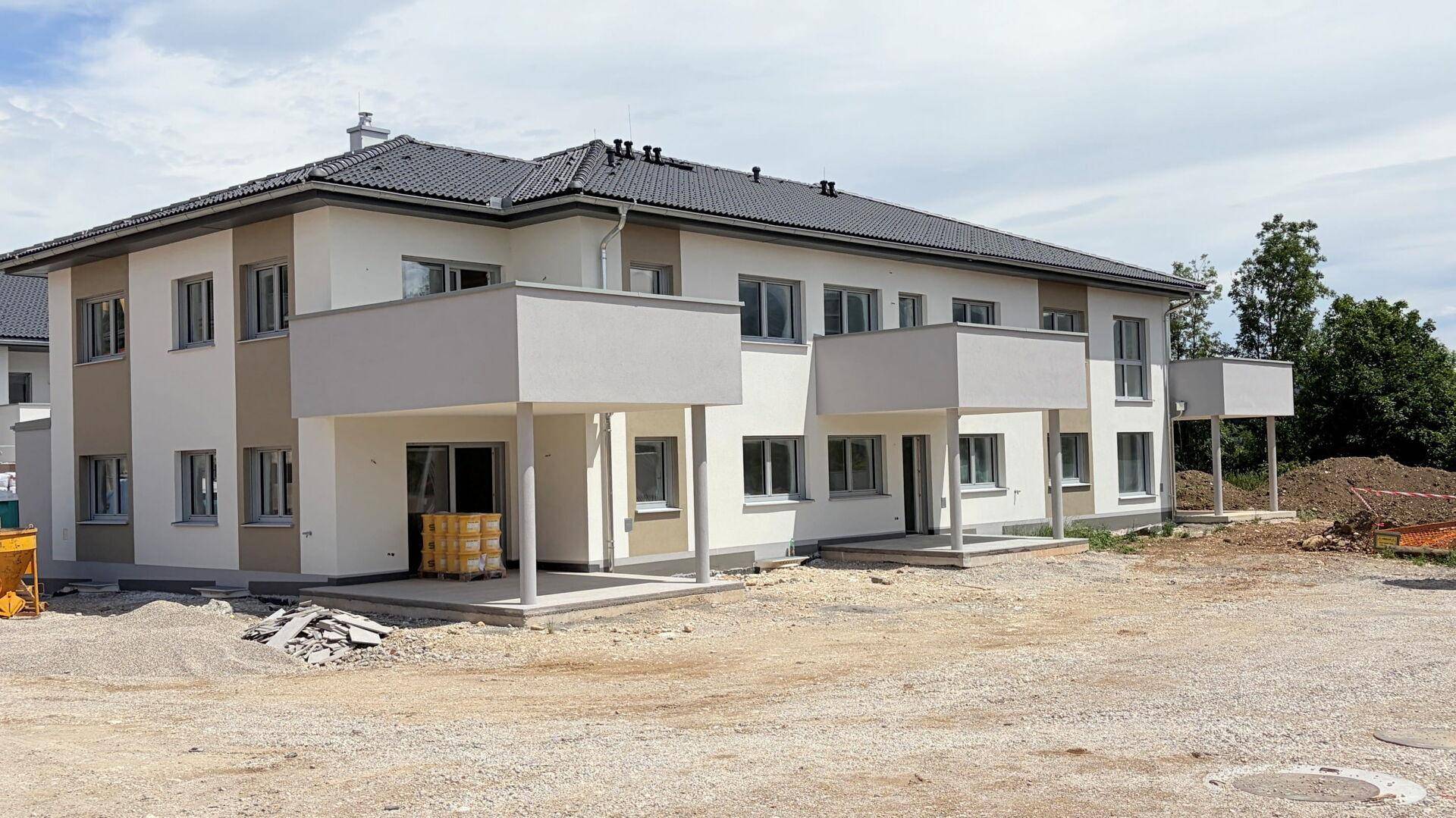 Neubau-Mehrfamilienhaus mit Balkonen und Terrassen, umgeben von einer Baustelle.