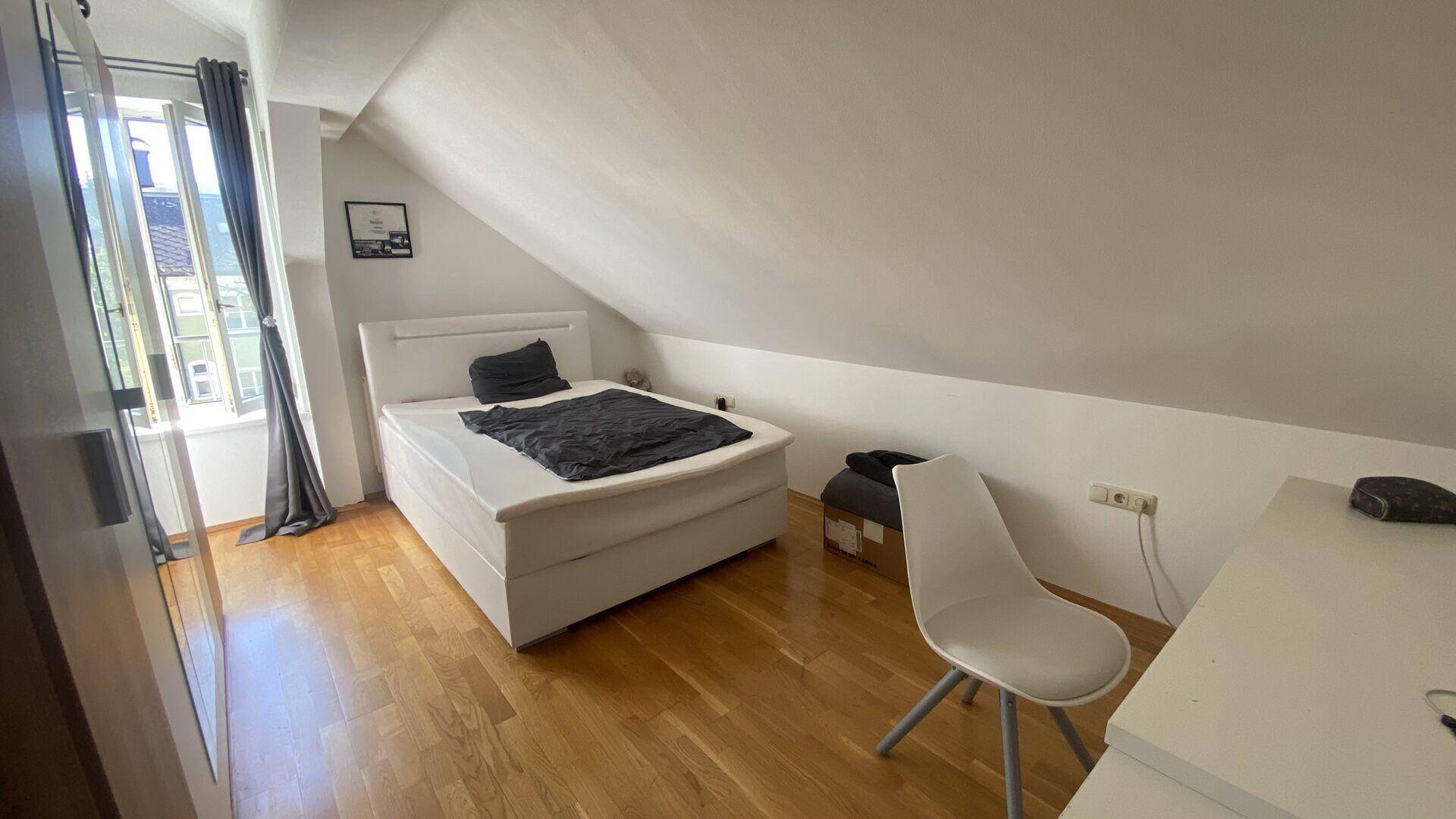 Helles Schlafzimmer im Dachgeschoss mit Holzboden, Doppelbett und schrägen Wänden.