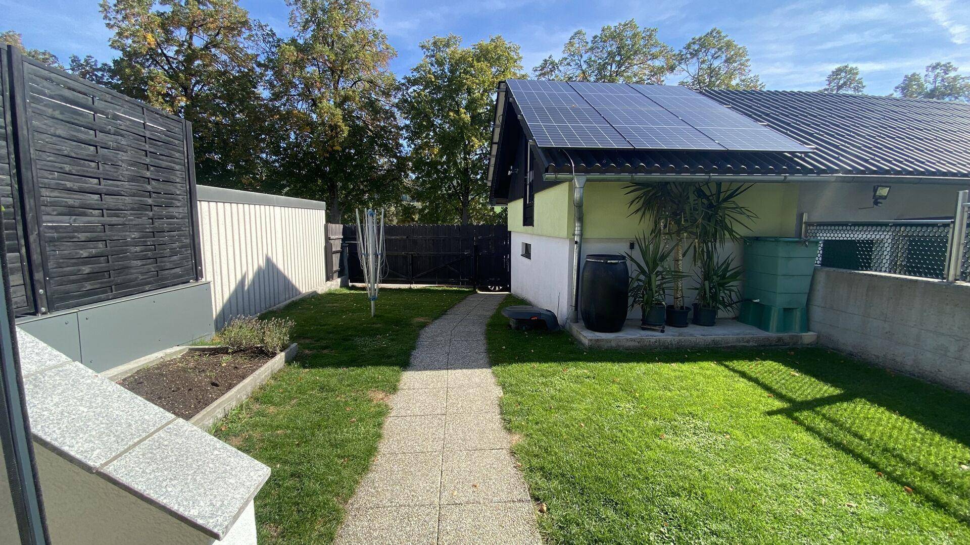 Gepflegter Garten mit Rasenfläche, Gehweg und Photovoltaikanlage auf dem Dach.