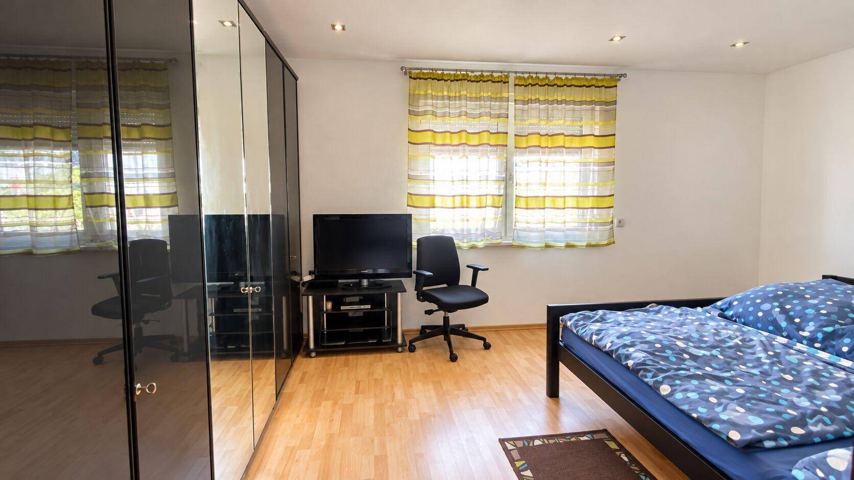 Schlafzimmer mit Laminatboden, großem Spiegelschrank und Blick ins Grüne.
