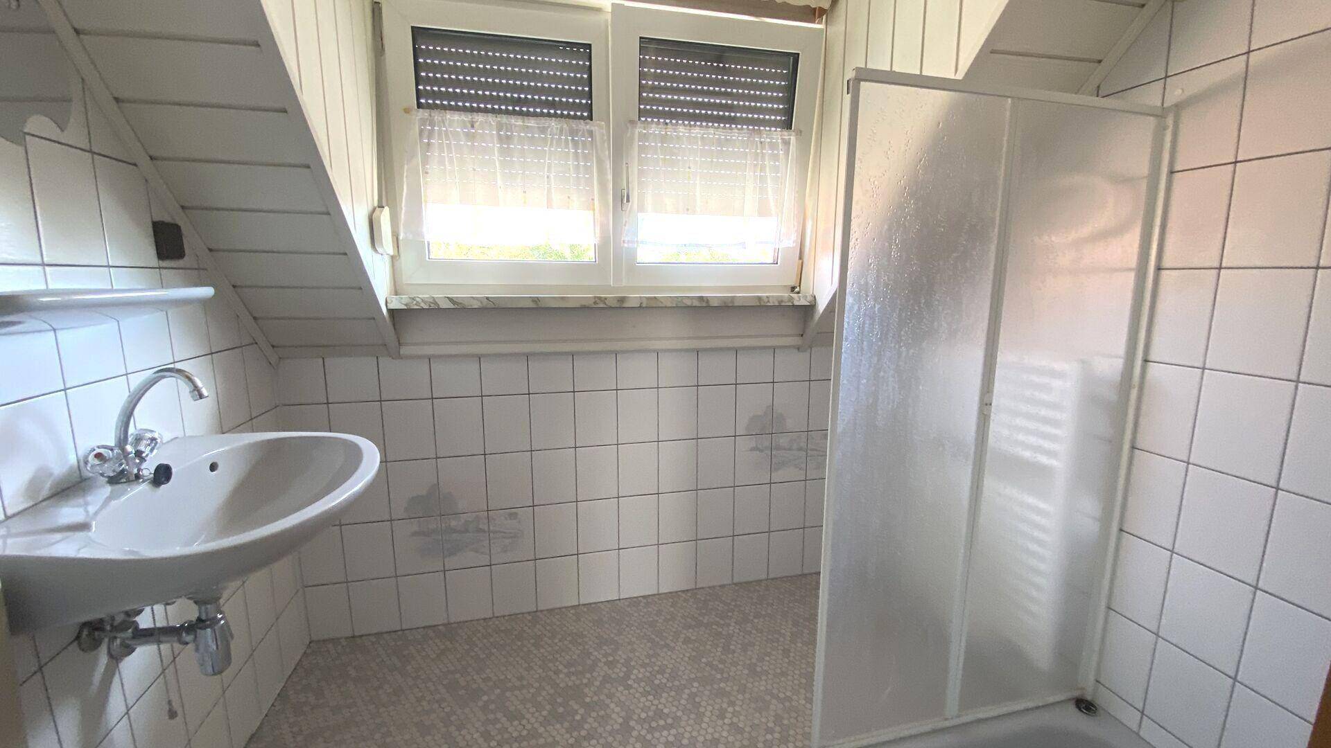 Dachgeschoss-Badezimmer mit Dusche, Waschbecken und weißen Fliesen, unter der Dachschräge.