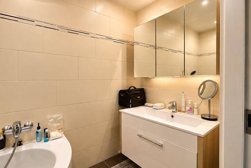 Badezimmer mit Einzelwaschbecken, Spiegelschrank und beigefarbenen Wandfliesen.