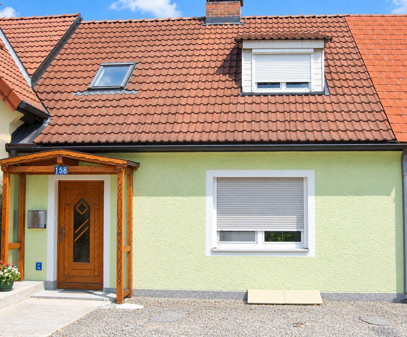 Vorderansicht des Hauses mit traditionellem Ziegeldach und Rollläden an den Fenstern.