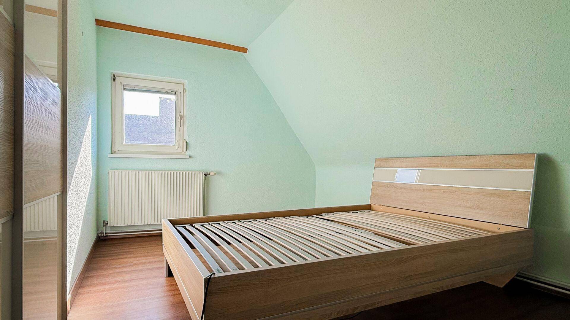 Schlafzimmer im Dachgeschoss mit mintgrünen Wänden, Holzbettrahmen und Laminatboden.