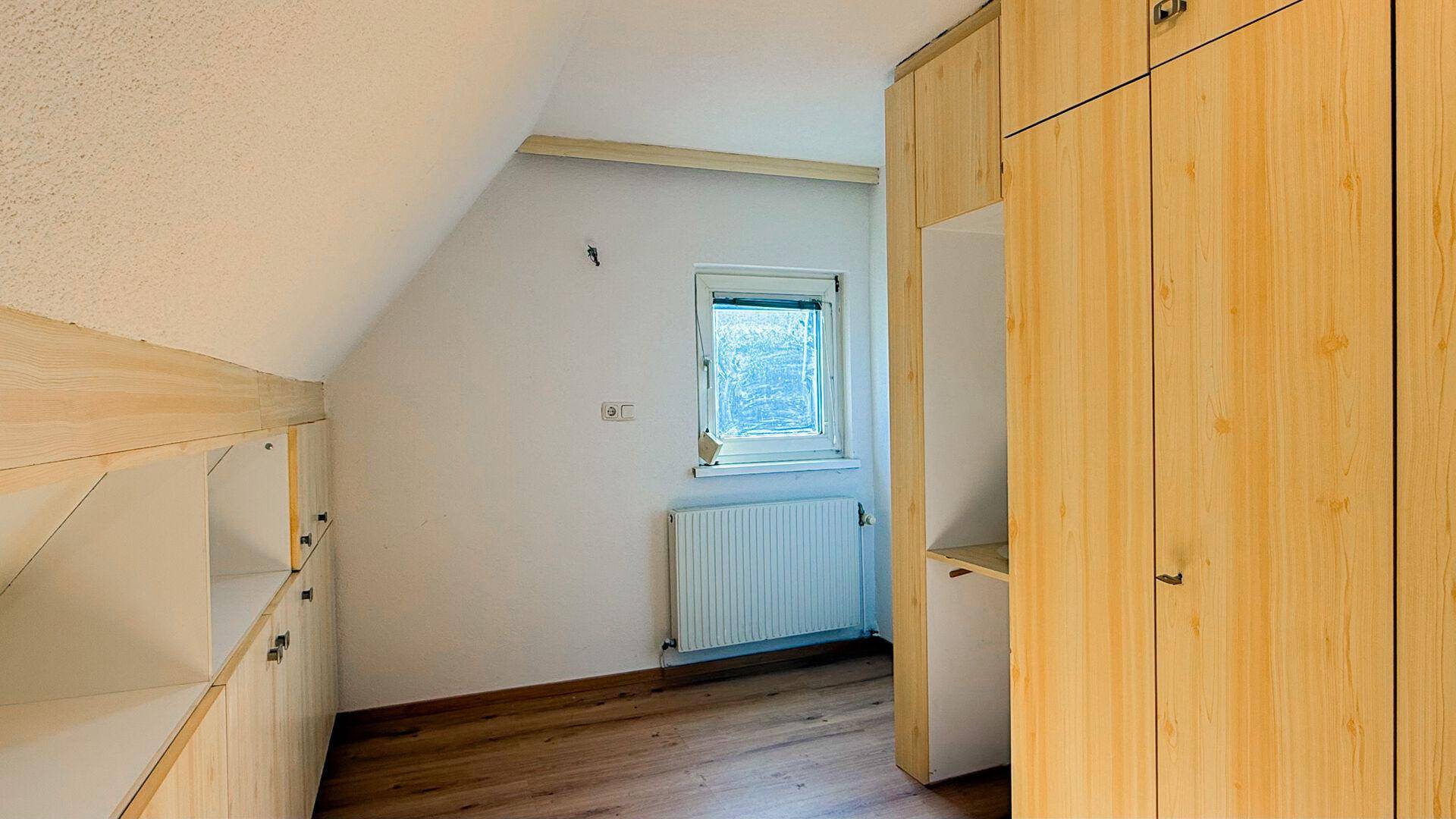 Helles Dachzimmer mit Einbauschränken, Laminatboden und einem Fenster.