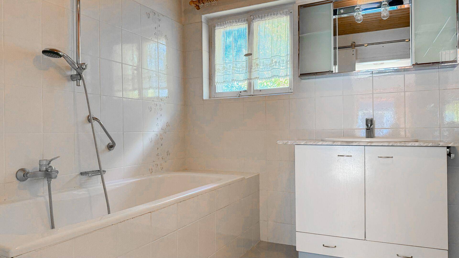 Badezimmer mit Badewanne, Duscharmatur, Waschbeckenunterschrank und Fenster.