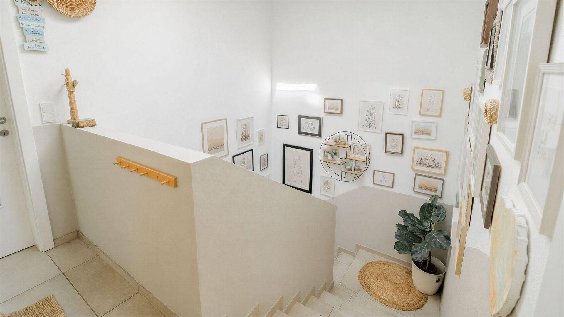Heller Treppenaufgang mit weiß gestrichenen Wänden und einer Galerie von gerahmten Bildern.
