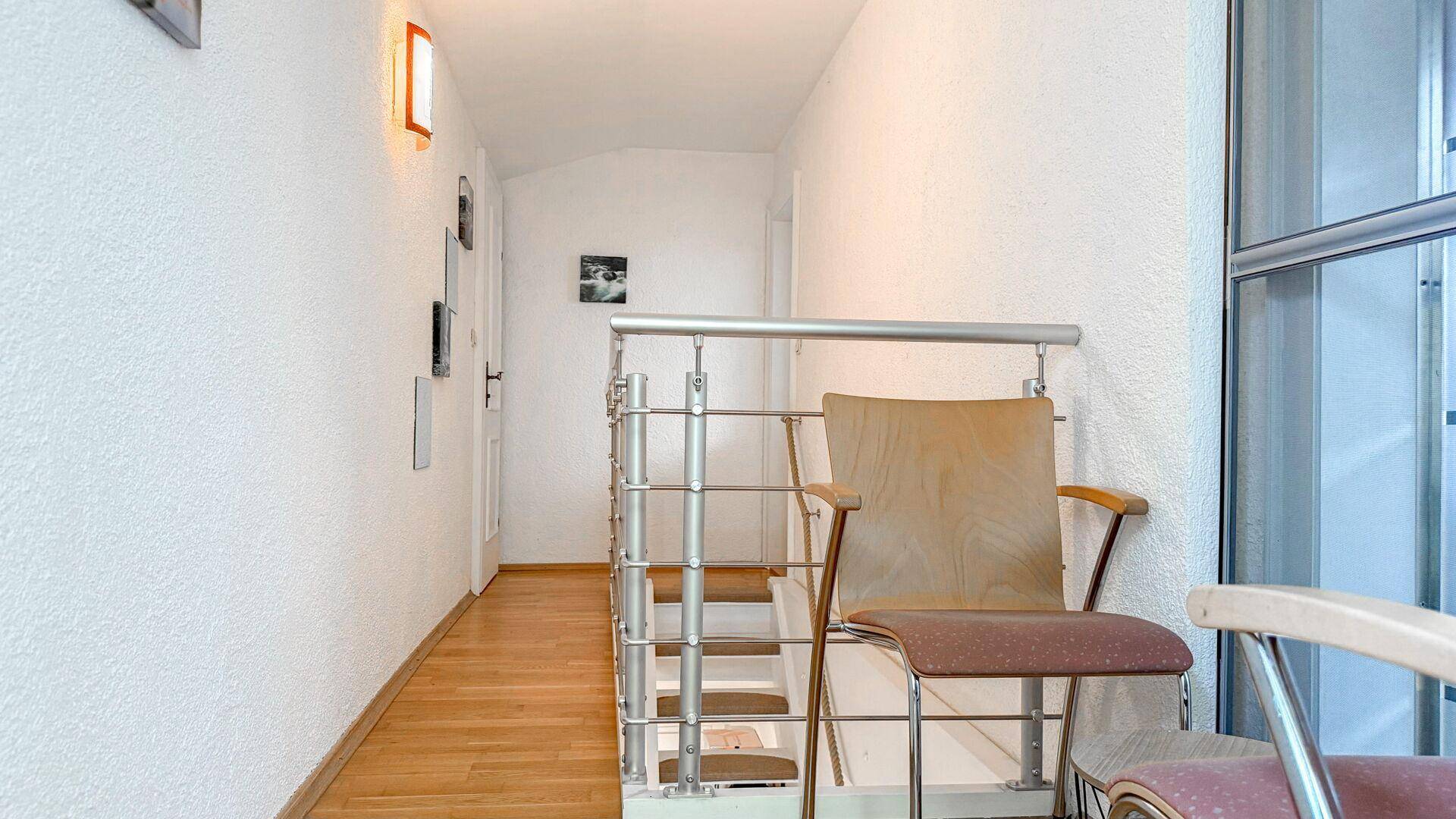 Heller Flur mit Holztreppe, Metallgeländer und Parkettboden.