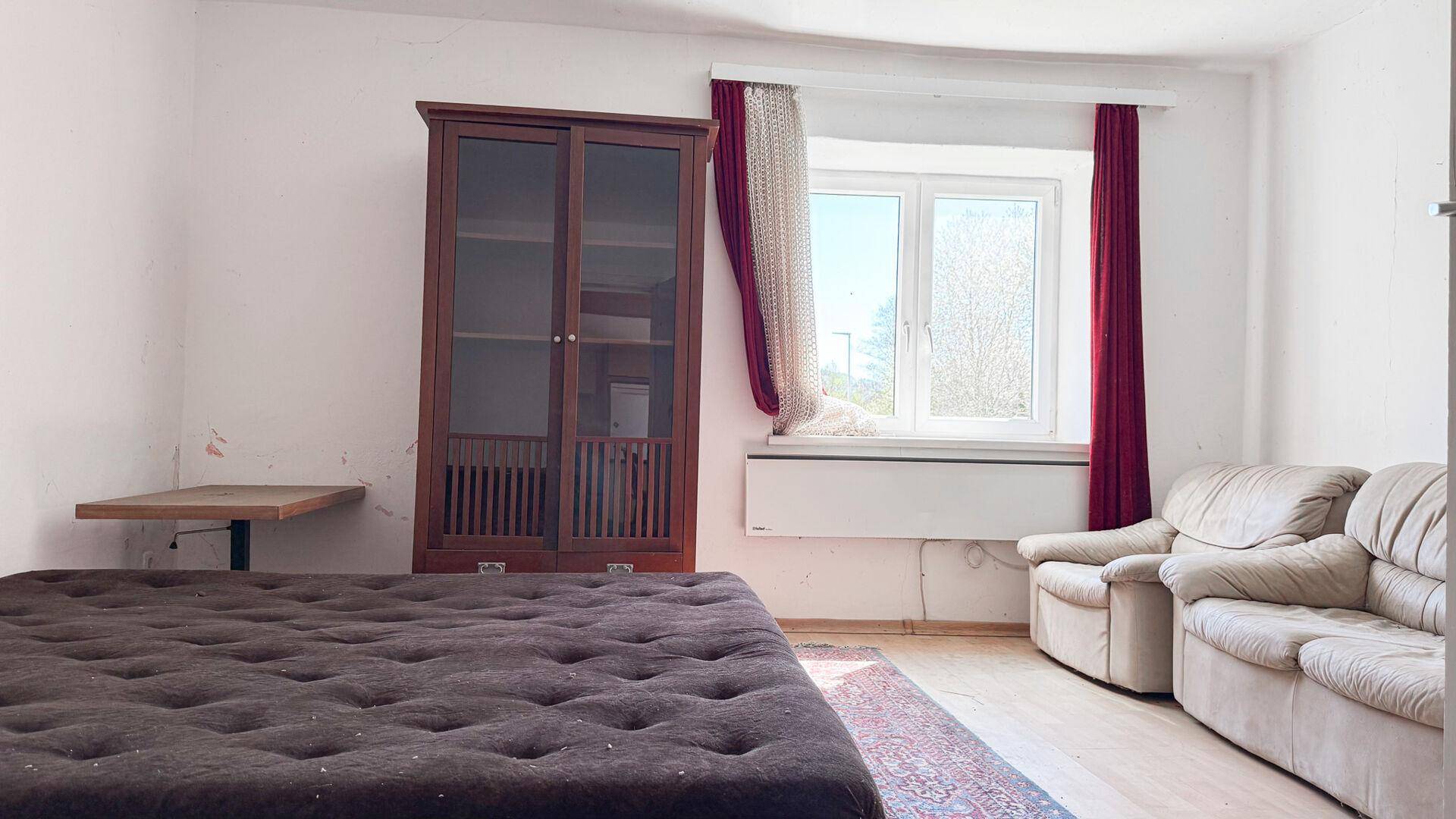Schlafzimmer mit Bett, Sessel und Schrank, gut belichtet durch ein großes Fenster.