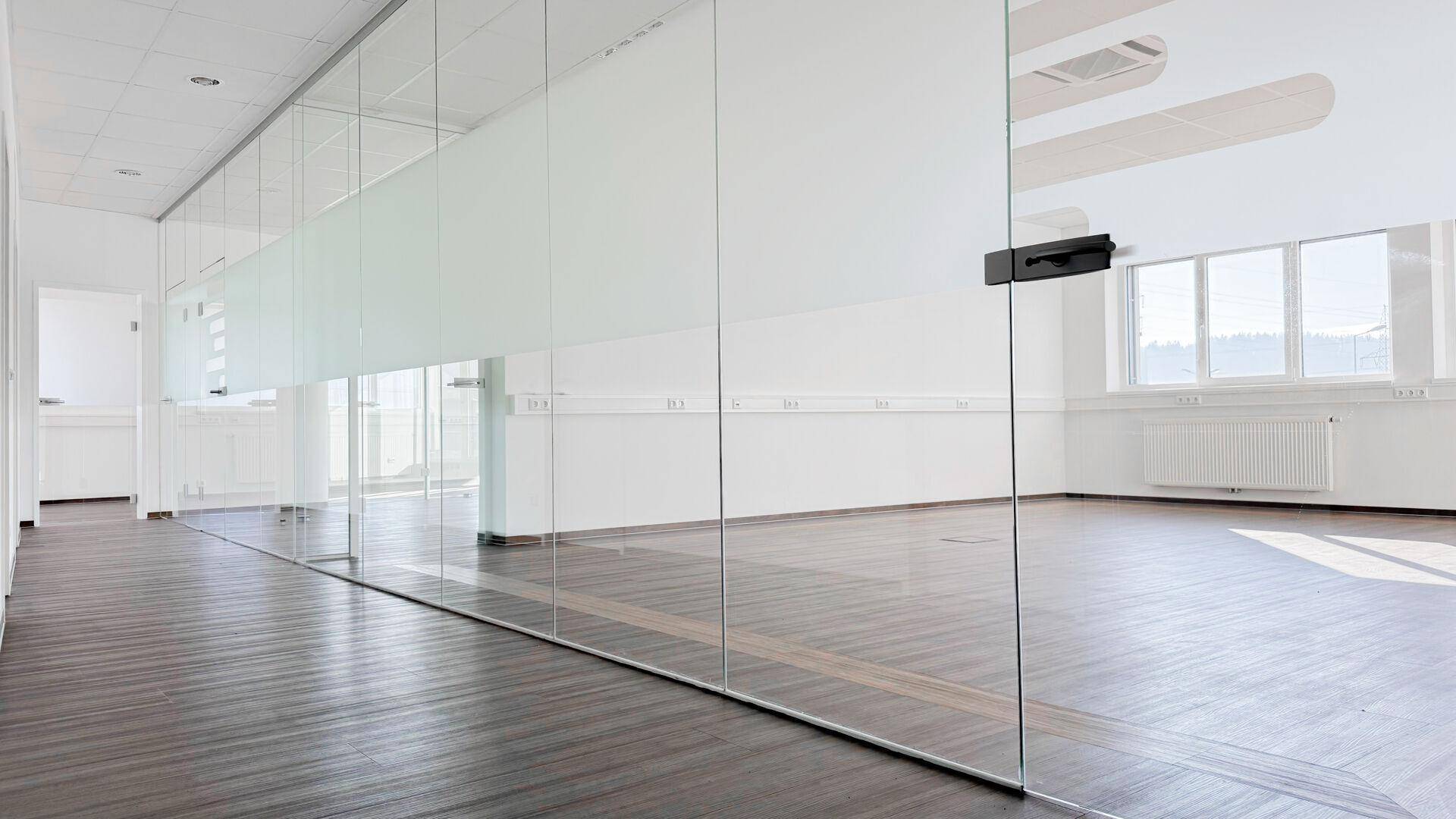 Heller Büroraum mit modernen Glaswänden und dunklem Laminatboden, ideal für eine offene Arbeitsumgebung.