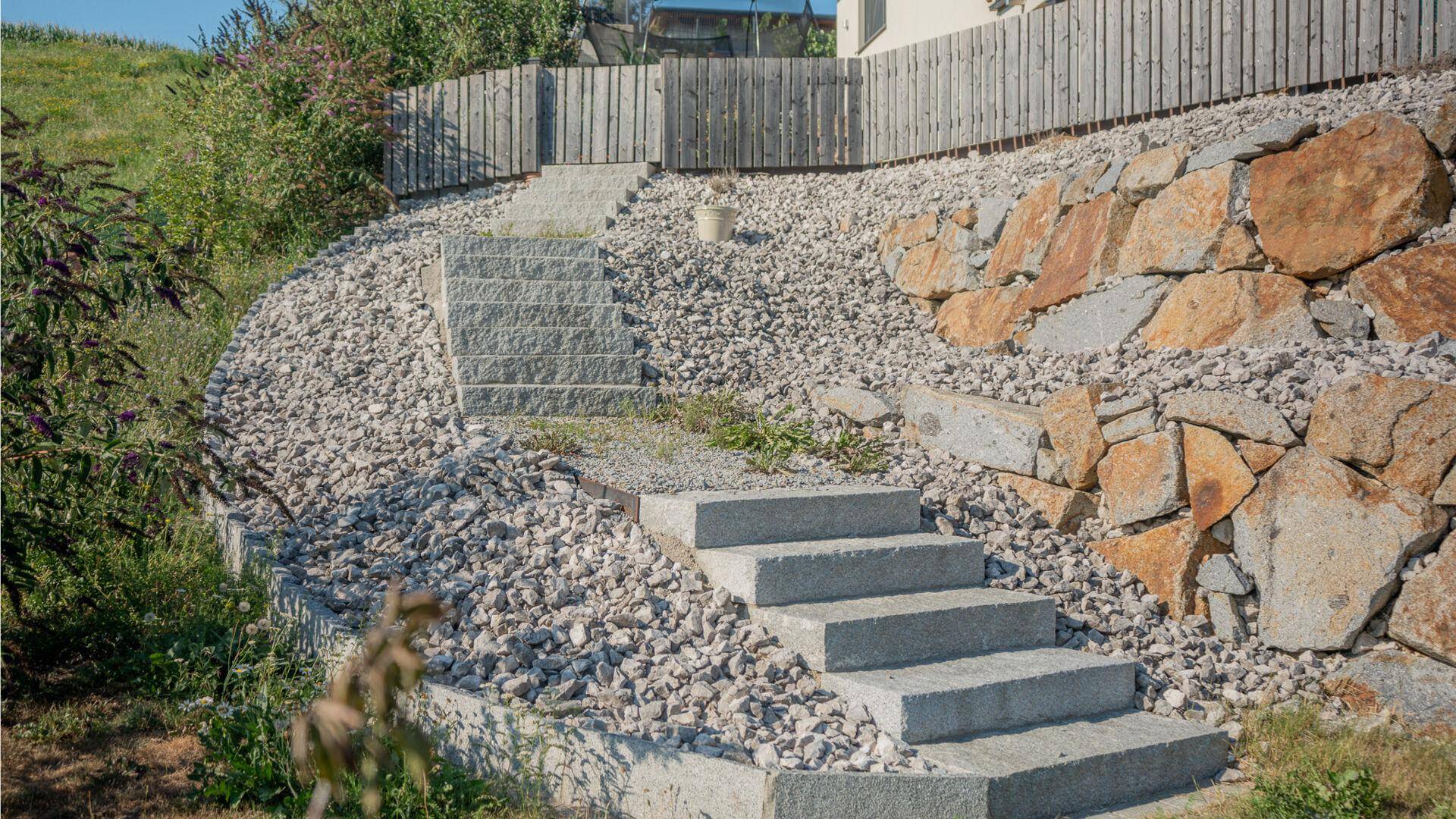 Steintreppe im terrassierten Garten mit Kiesflächen und Natursteinmauern, robust und pflegeleicht.