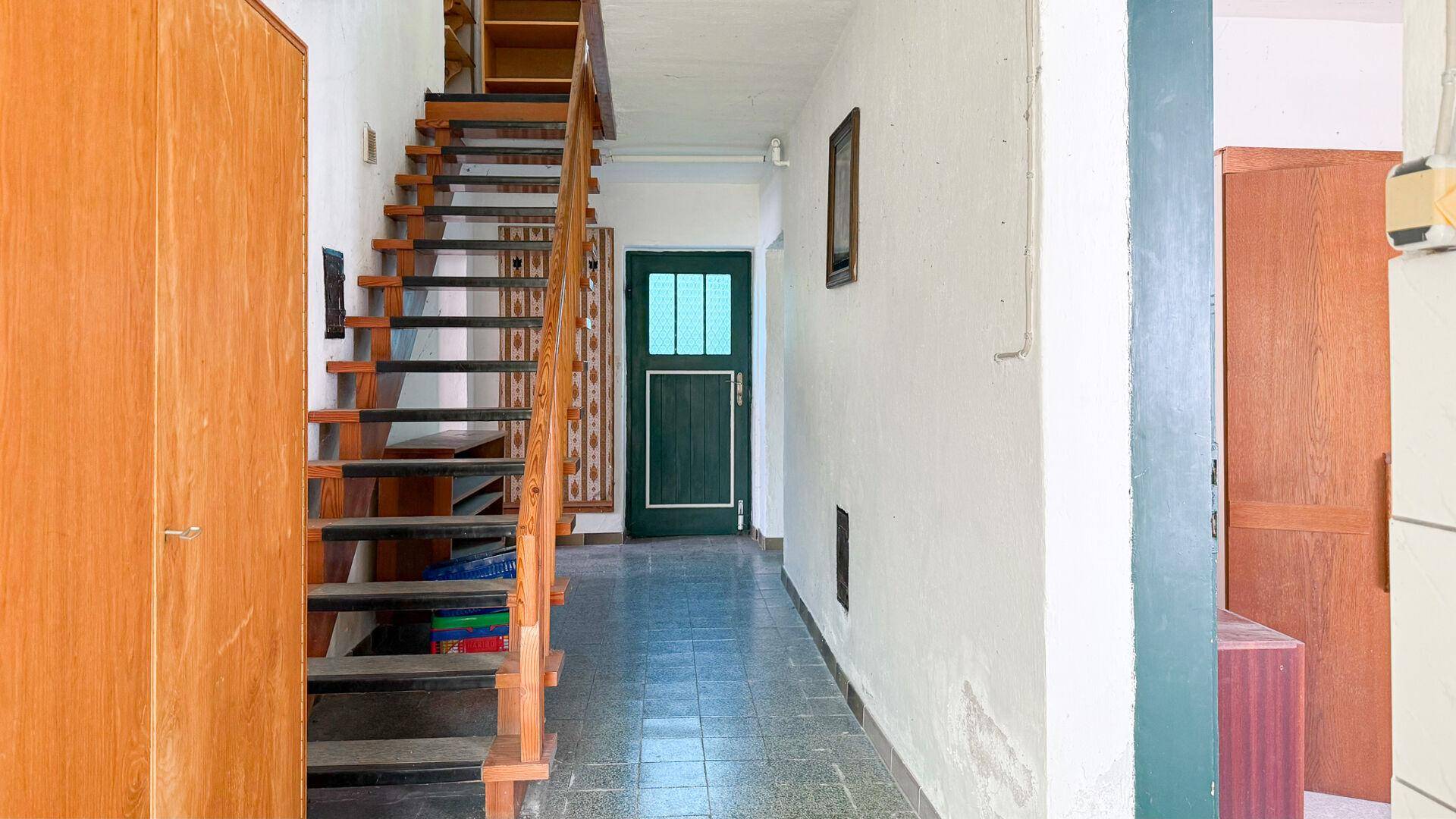 Heller Flur mit Holztreppe und gefliestem Boden, der zu den oberen Etagen führt.
