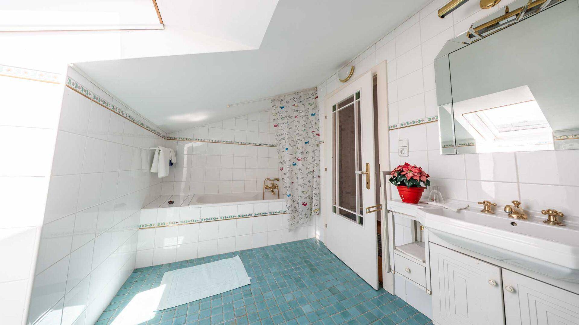 Badezimmer im Dachgeschoss mit blauen und weißen Fliesen, Badewanne und Dachfenster.