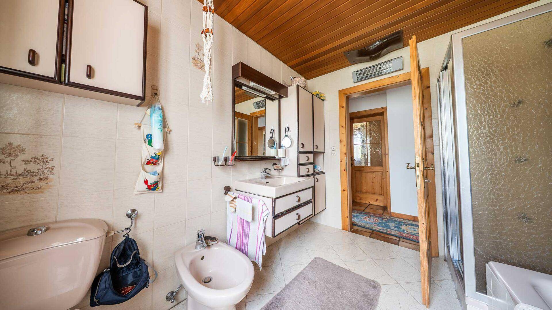 Badezimmer im 80er-Jahre-Stil mit beigen Fliesen, Bidet und Duschkabine.