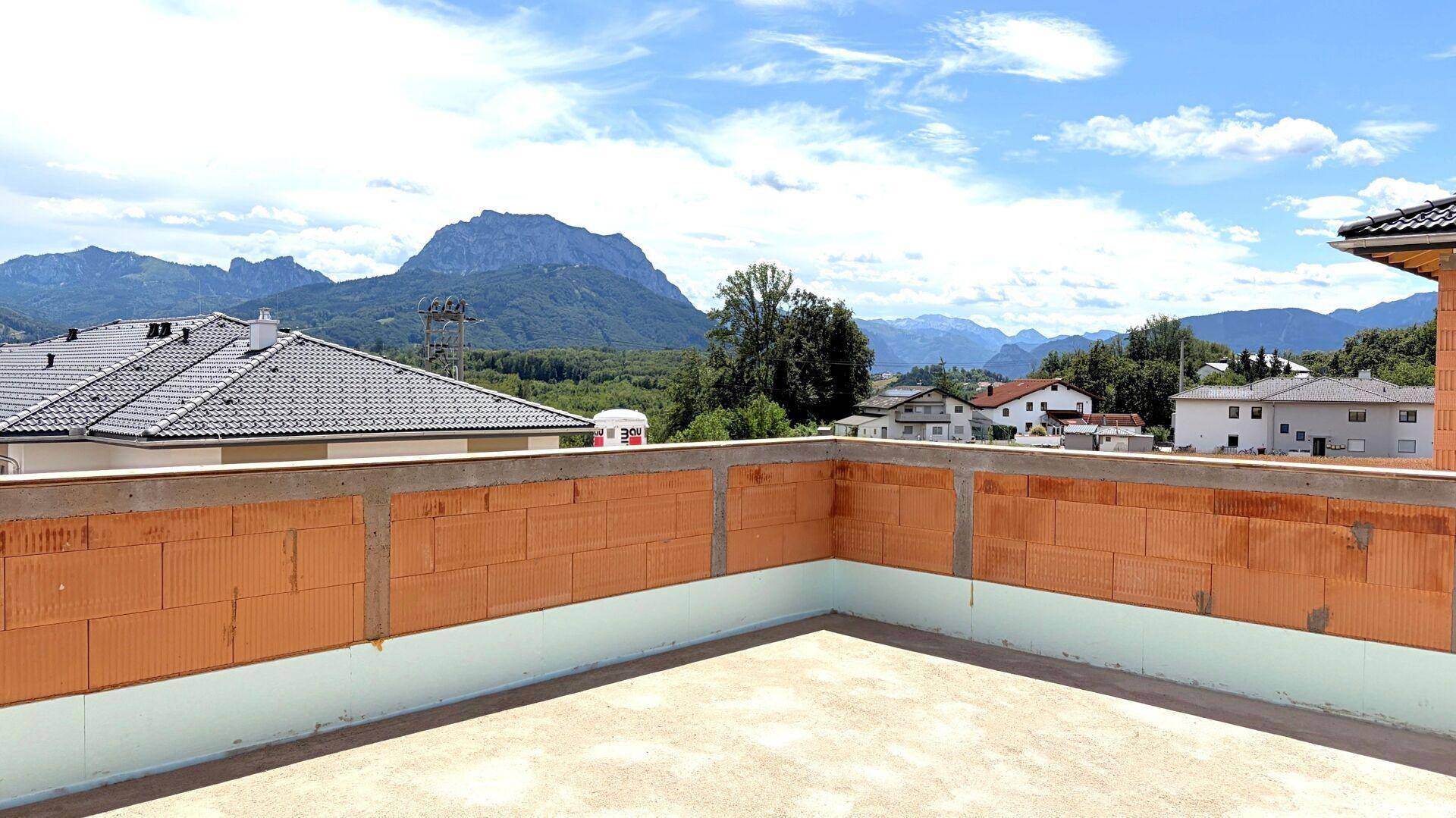 Unfertige Dachterrasse mit Ziegelwänden und weitem Blick auf die Berge und die umliegende Bebauung.