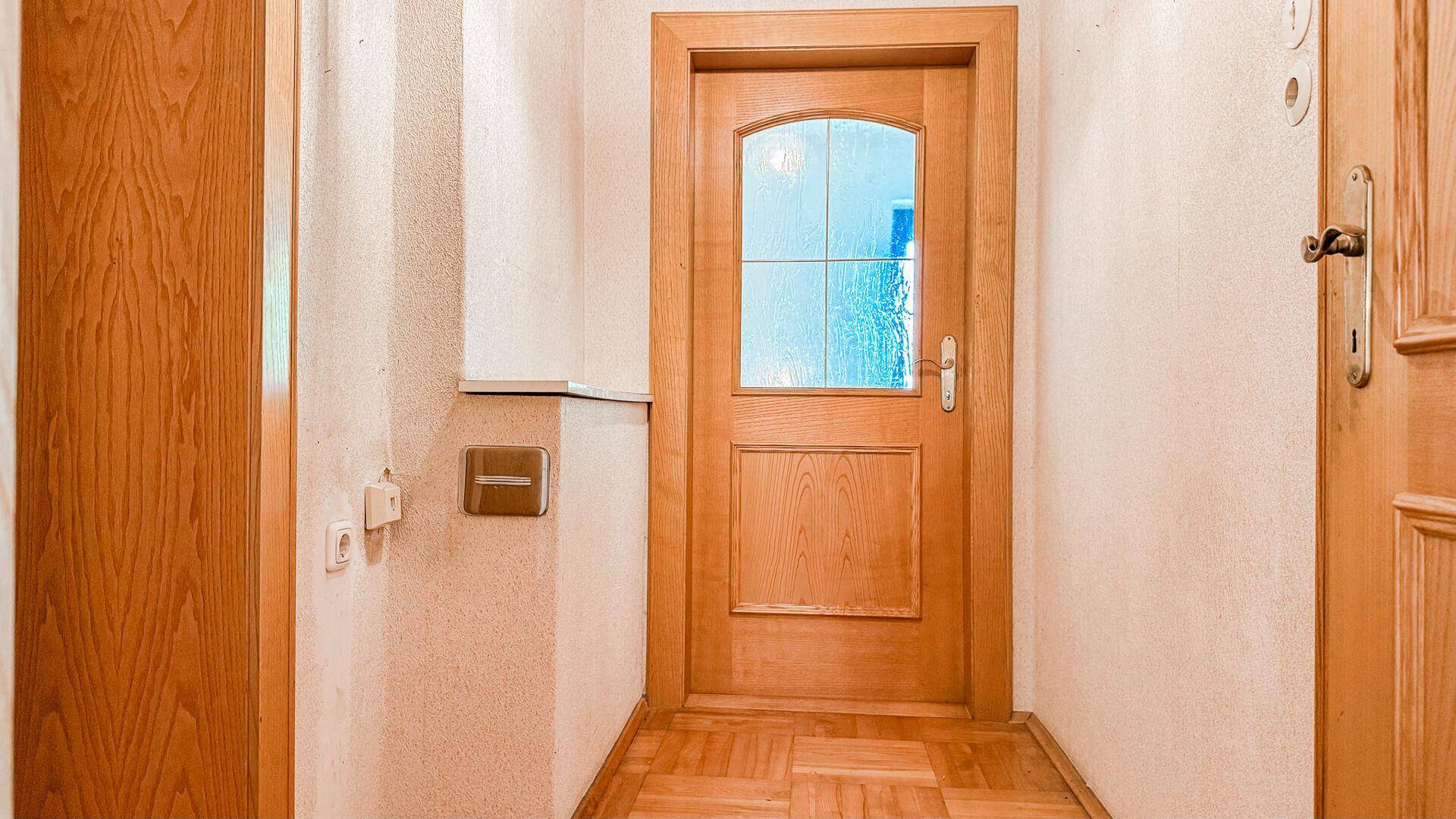 Heller Flur mit Parkettboden und einer Holztür mit Glaseinsatz, die zum nächsten Raum führt.
