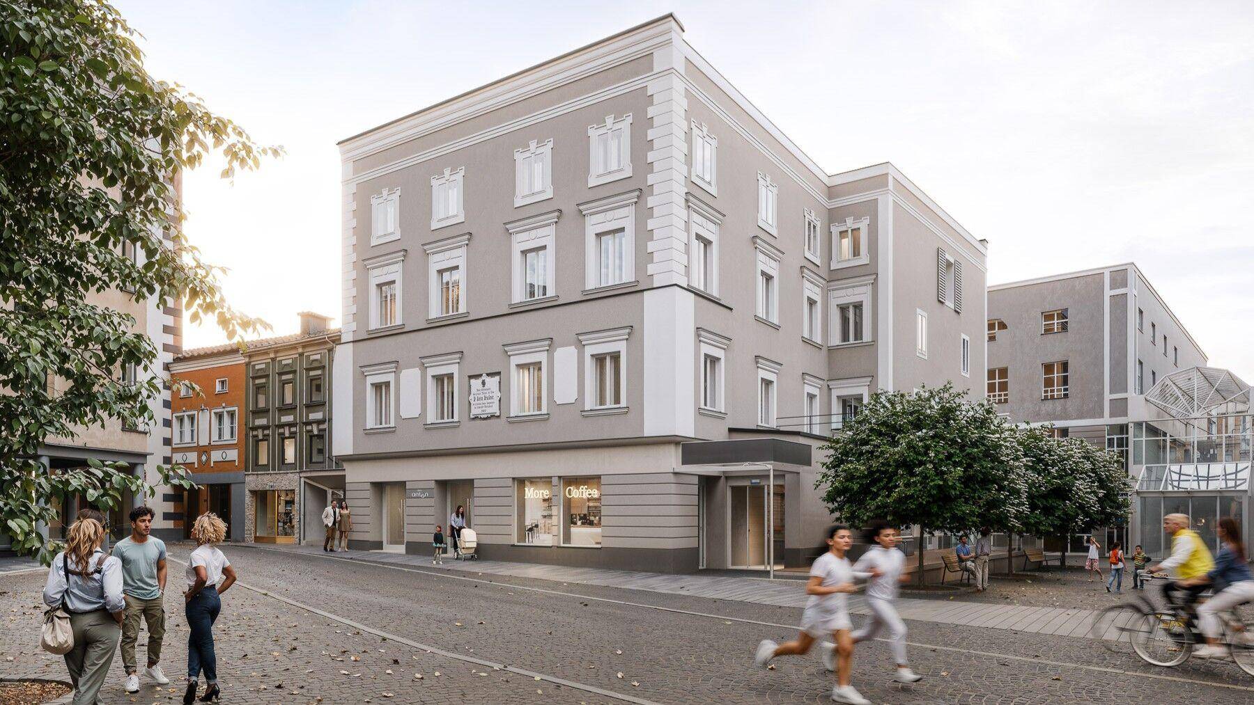 Historisches Gebäude mit modernisierter Fassade und Geschäften im Erdgeschoss an einem belebten Stadtplatz.