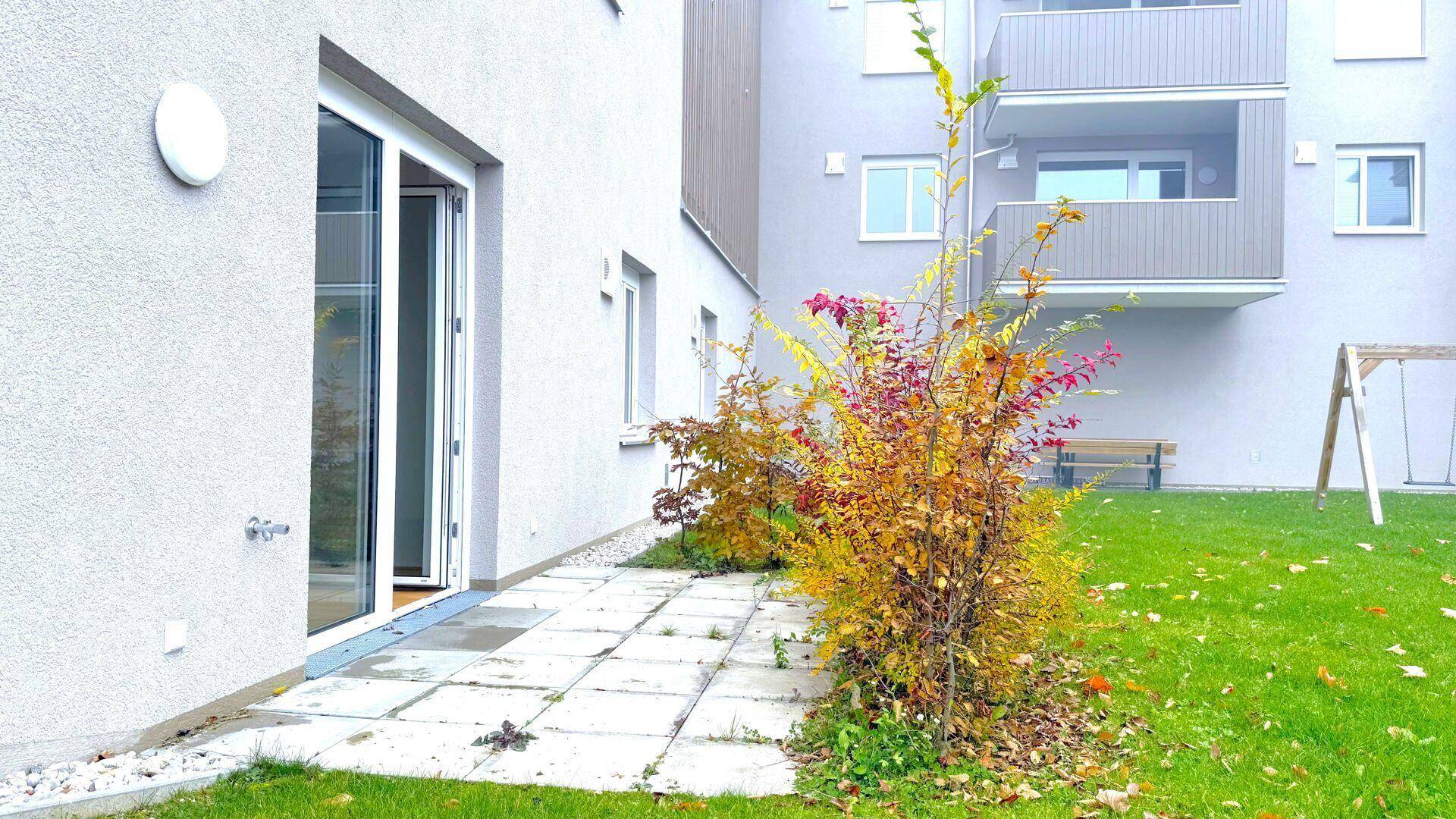 Kleine Terrasse mit Zugang zum Garten und einem Spielplatz im Hintergrund, umgeben von Herbstlaub.