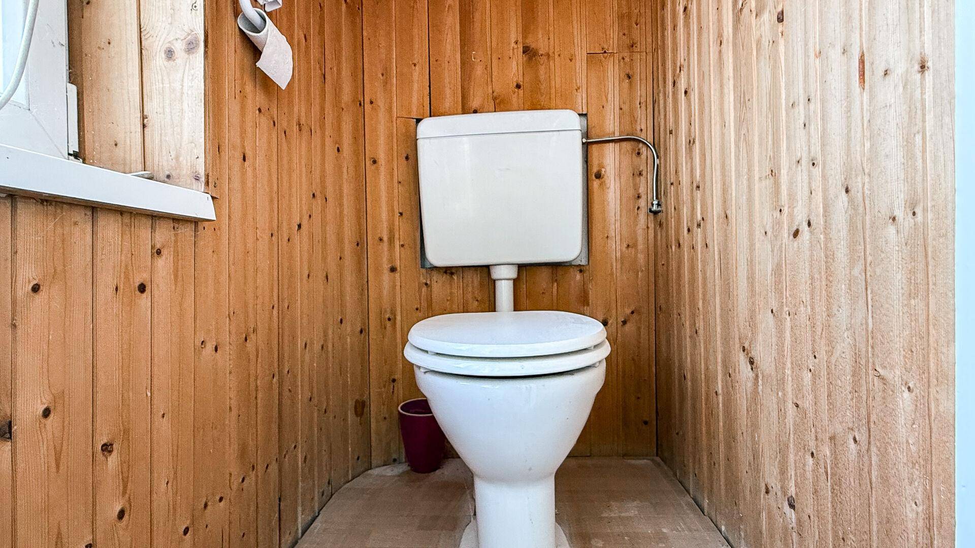 Einfaches WC mit Holzverkleidung an den Wänden und einem Fensterrahmen.