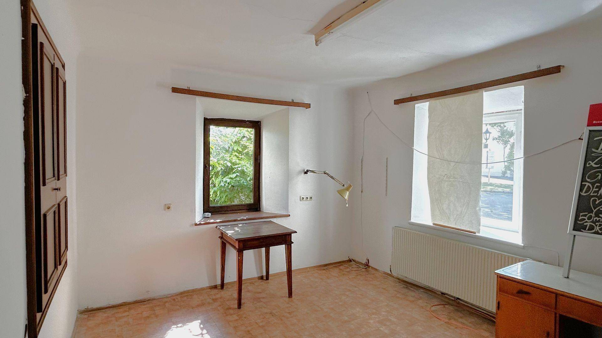Einfacher Raum mit Fensterblick ins Grüne, Heizkörper und einem kleinen Tisch.