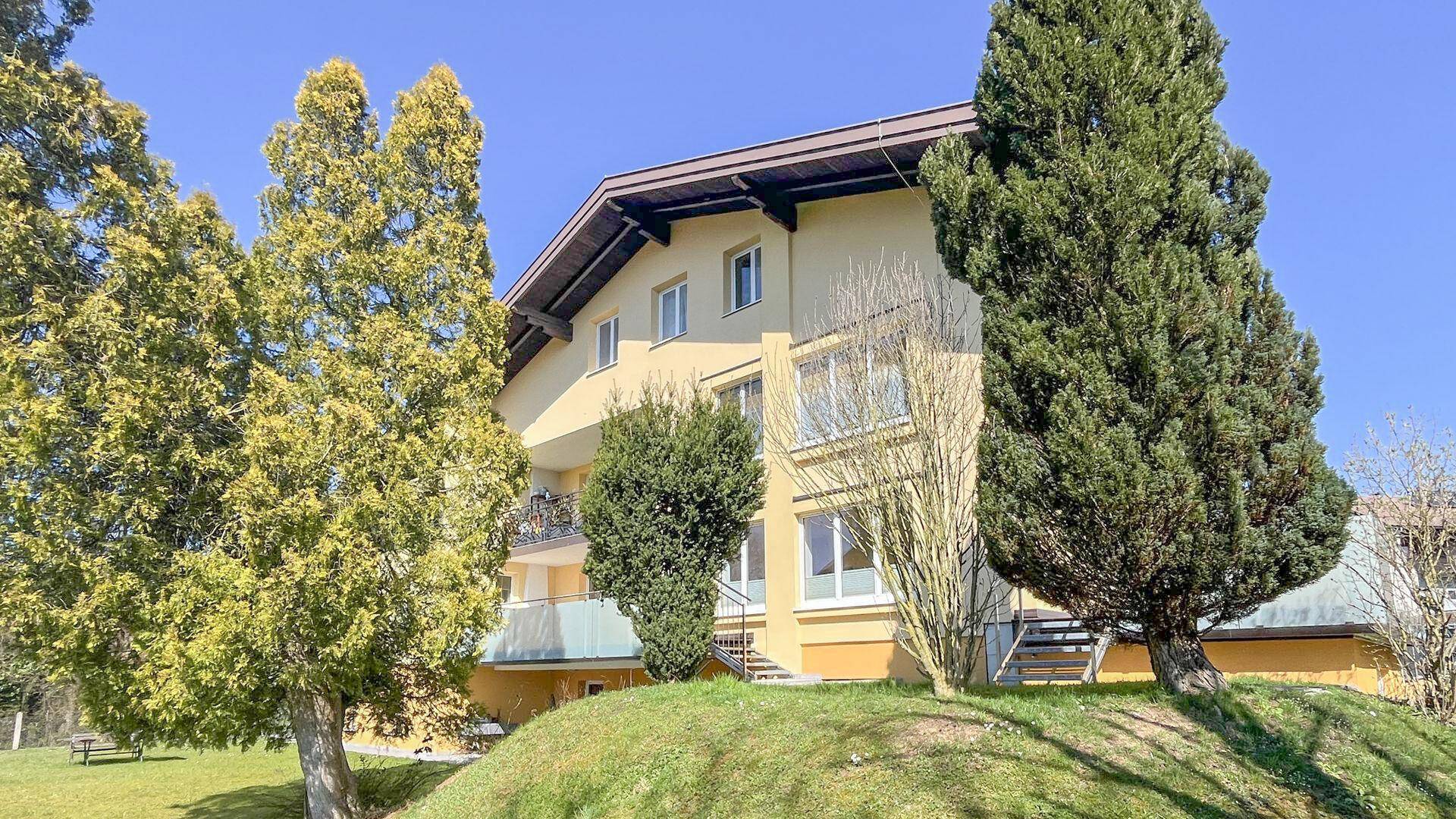 Gelbes Mehrfamilienhaus mit mehreren Balkonen, umgeben von Bäumen und Grünflächen.