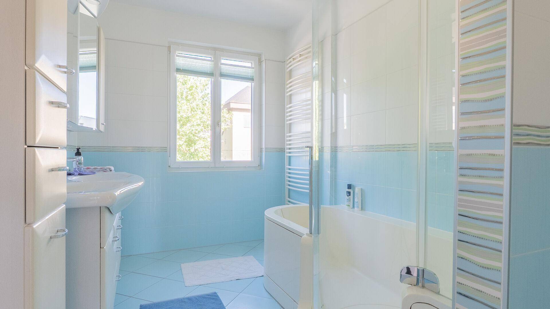 Badezimmer mit blauen Fliesen, Badewanne, Dusche und Fenster für Tageslicht.