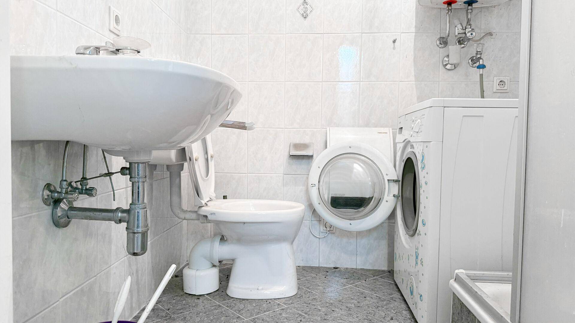 Badezimmer mit WC, Waschbecken und Waschmaschine, gefliest in hellen Farbtönen.