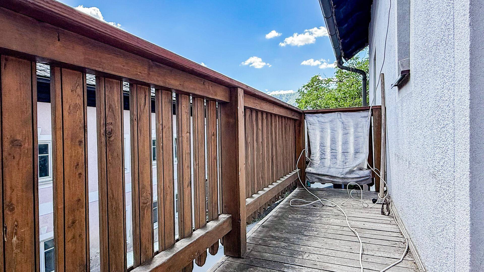 Rustikaler Holzbalkon mit Geländer und Blick auf die umliegende grüne Landschaft unter blauem Himmel.