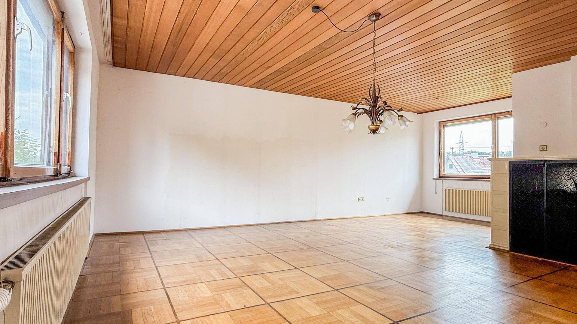 Geräumiges Wohnzimmer mit Holzdecke, Parkettboden und einem traditionellen Kachelofen.
