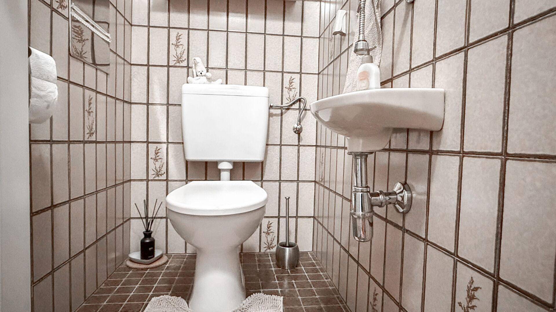 Kleines WC mit beigefarbenen Fliesen, Toilette und Handwaschbecken.