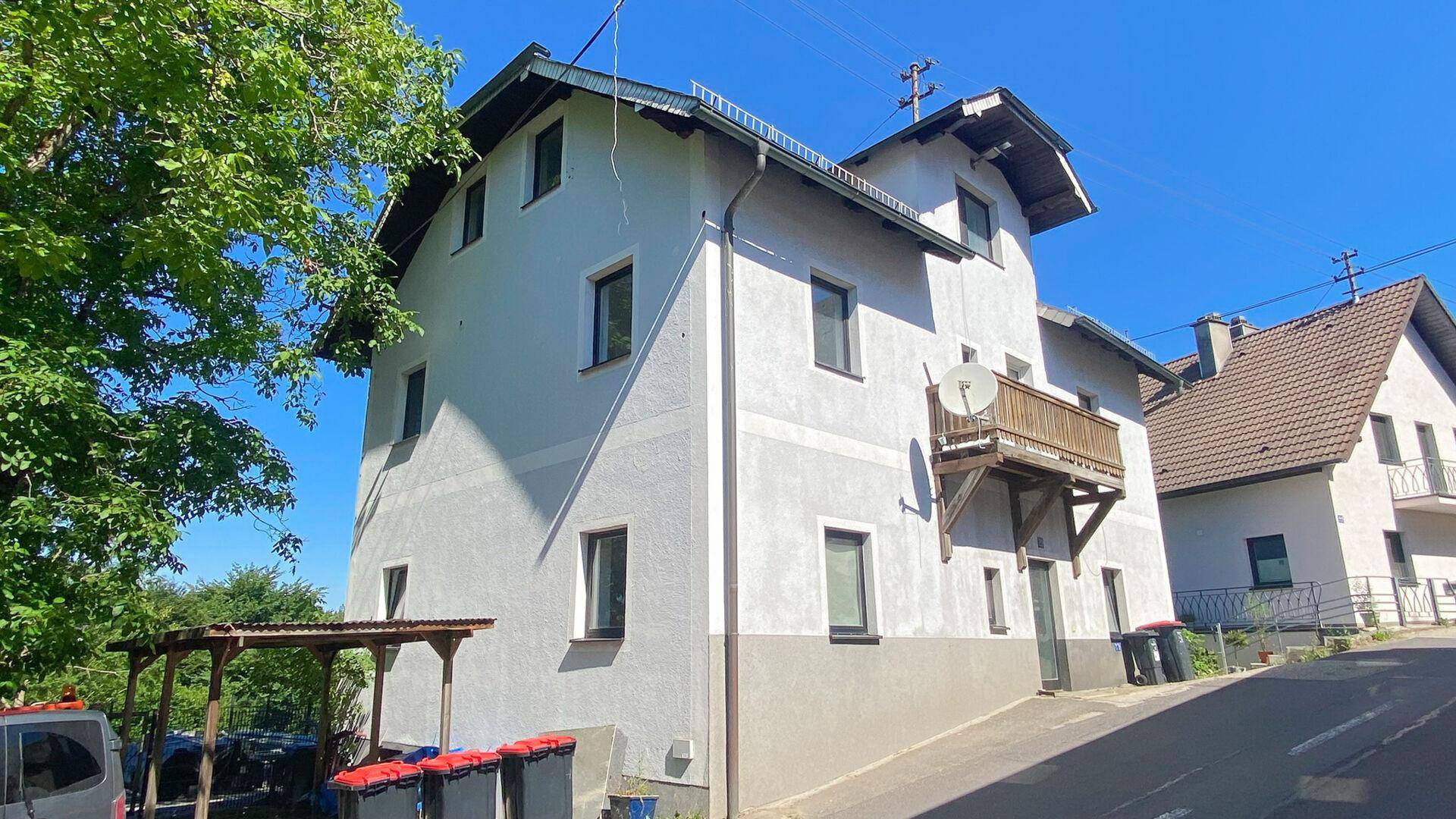 Mehrstöckiges Haus mit heller Fassade, kleinen Fenstern und einem Holzbalkon.