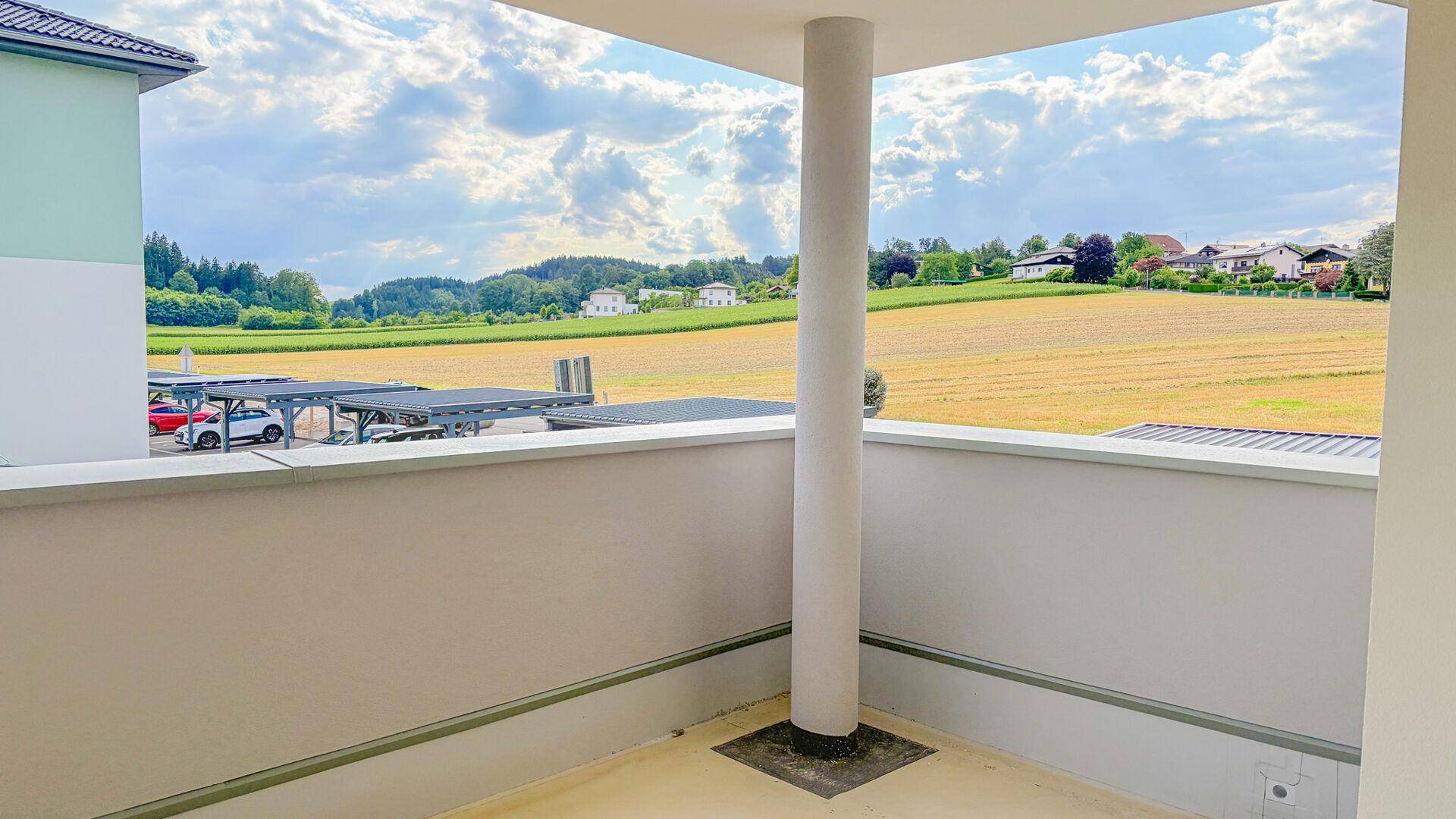 Überdachter Balkon mit weitem Blick über grüne Felder und die umliegende Landschaft.