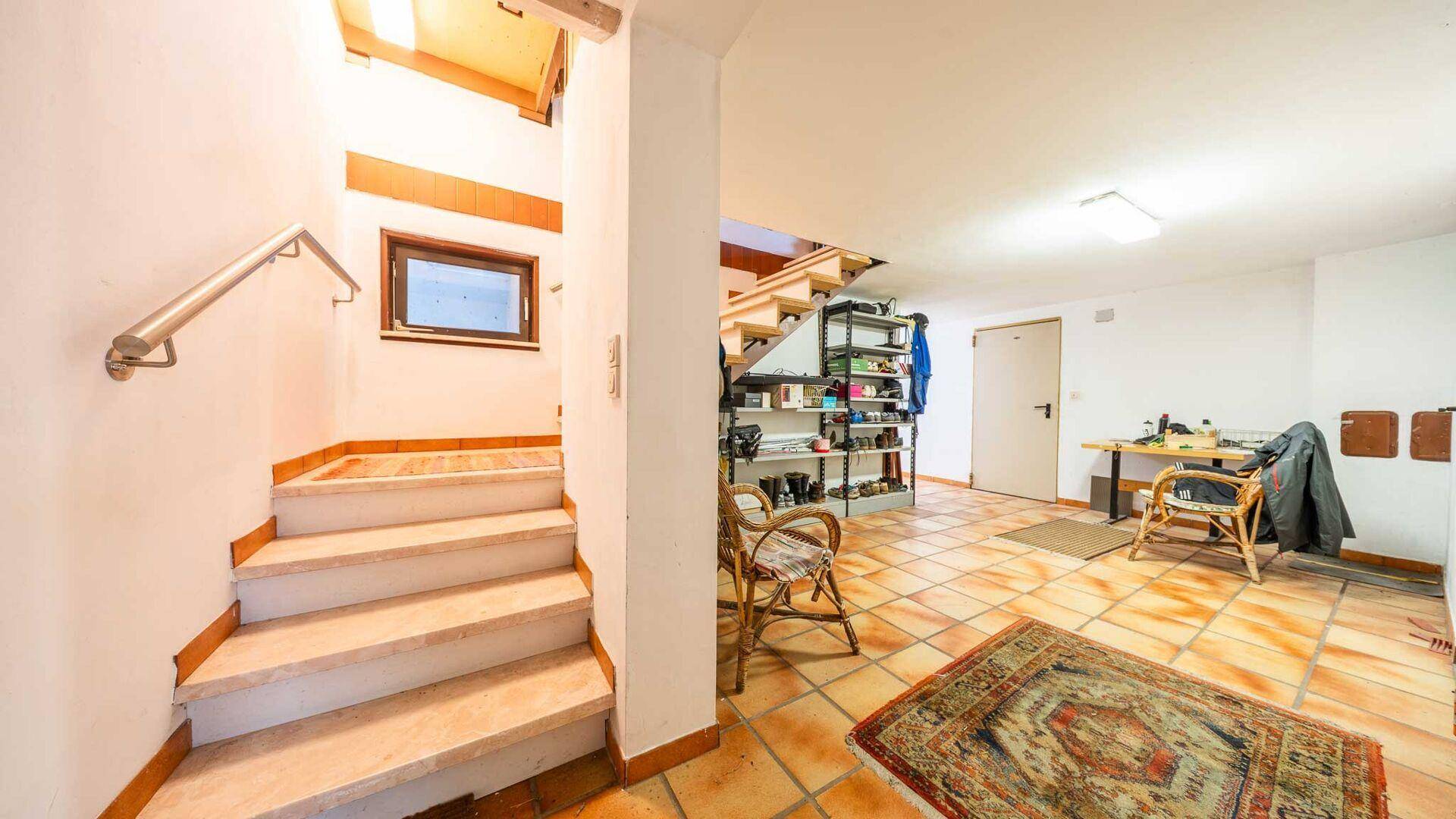 Heller Eingangsbereich mit gefliestem Boden, Treppe zum Obergeschoss und praktischen Regalen.