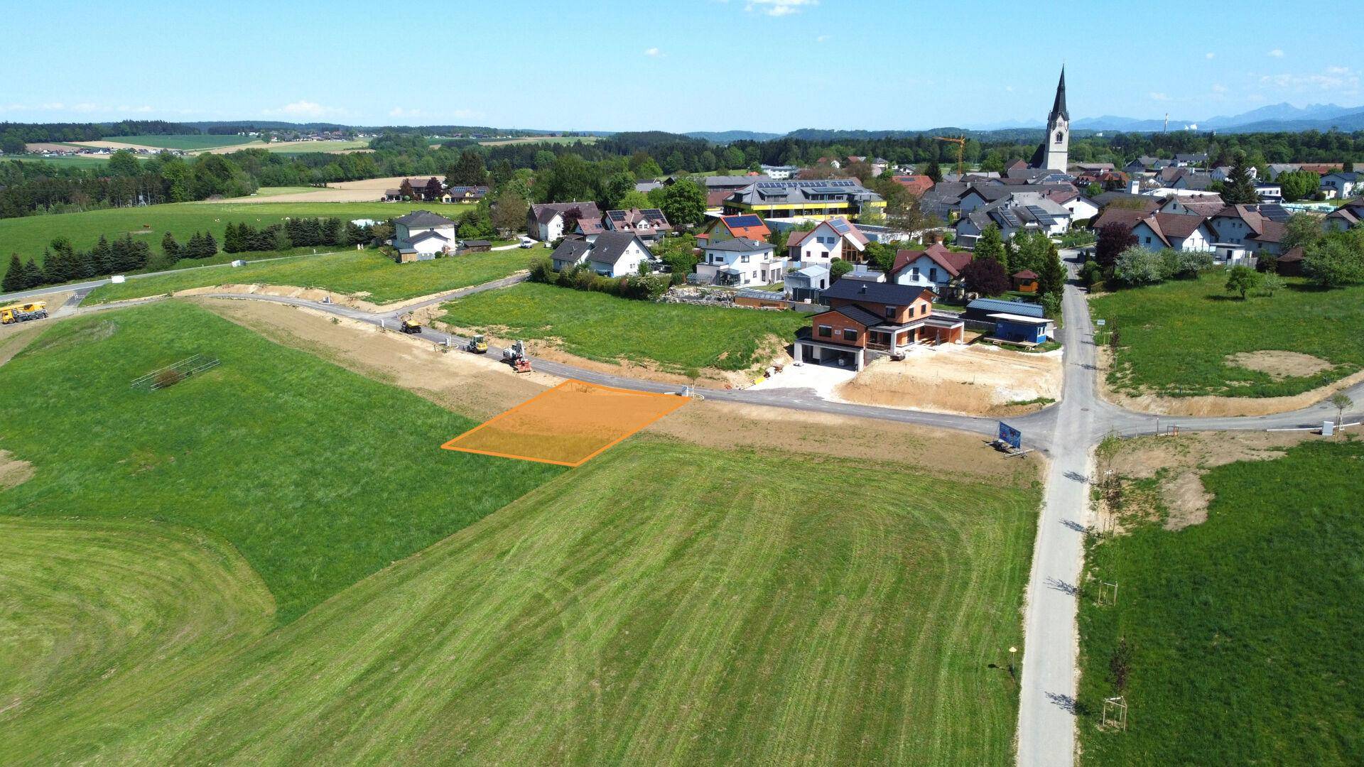 Luftaufnahme eines Baugrundstücks in einer ländlichen Umgebung mit angrenzendem Dorf und grünen Feldern.