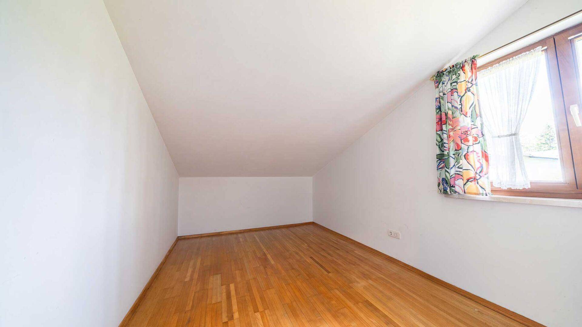 Leeres Zimmer im Dachgeschoss mit Holzparkett, Dachschräge und Fenster.