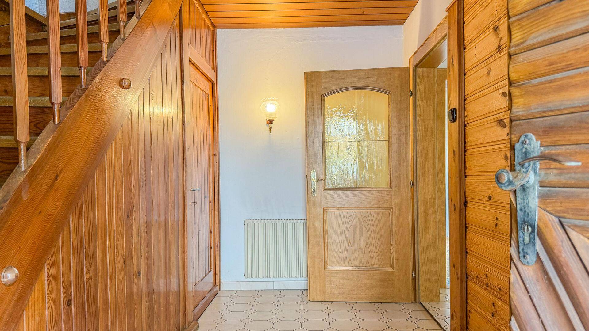 Flur mit Holzvertäfelung, Holztreppe und Fliesenboden, der einen rustikalen Charme verleiht.