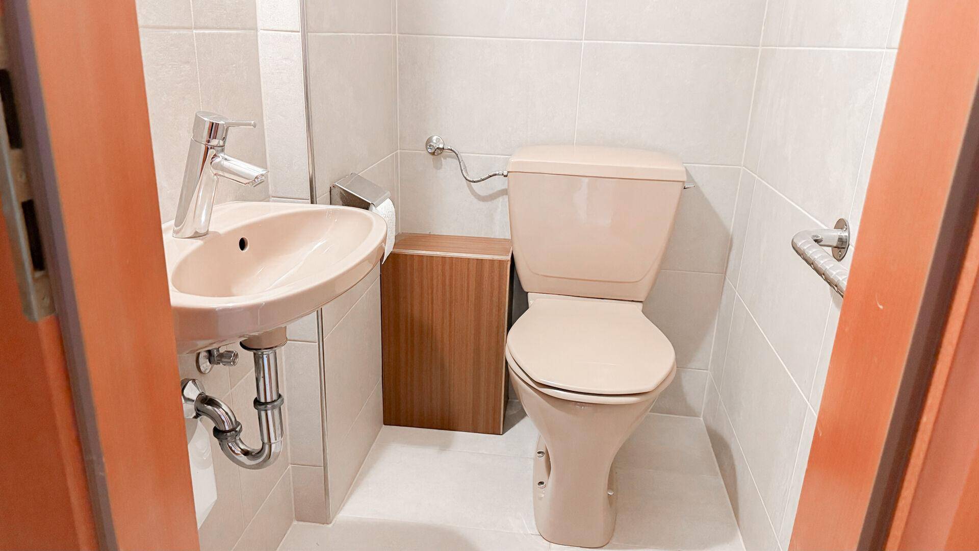 Kleines Gäste-WC mit beigefarbener Toilette, Waschbecken und hellen Fliesen.