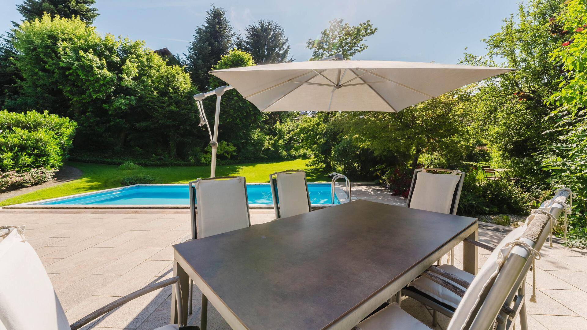 Sonniger Sitzbereich auf der Terrasse mit großem Sonnenschirm und Poolblick.