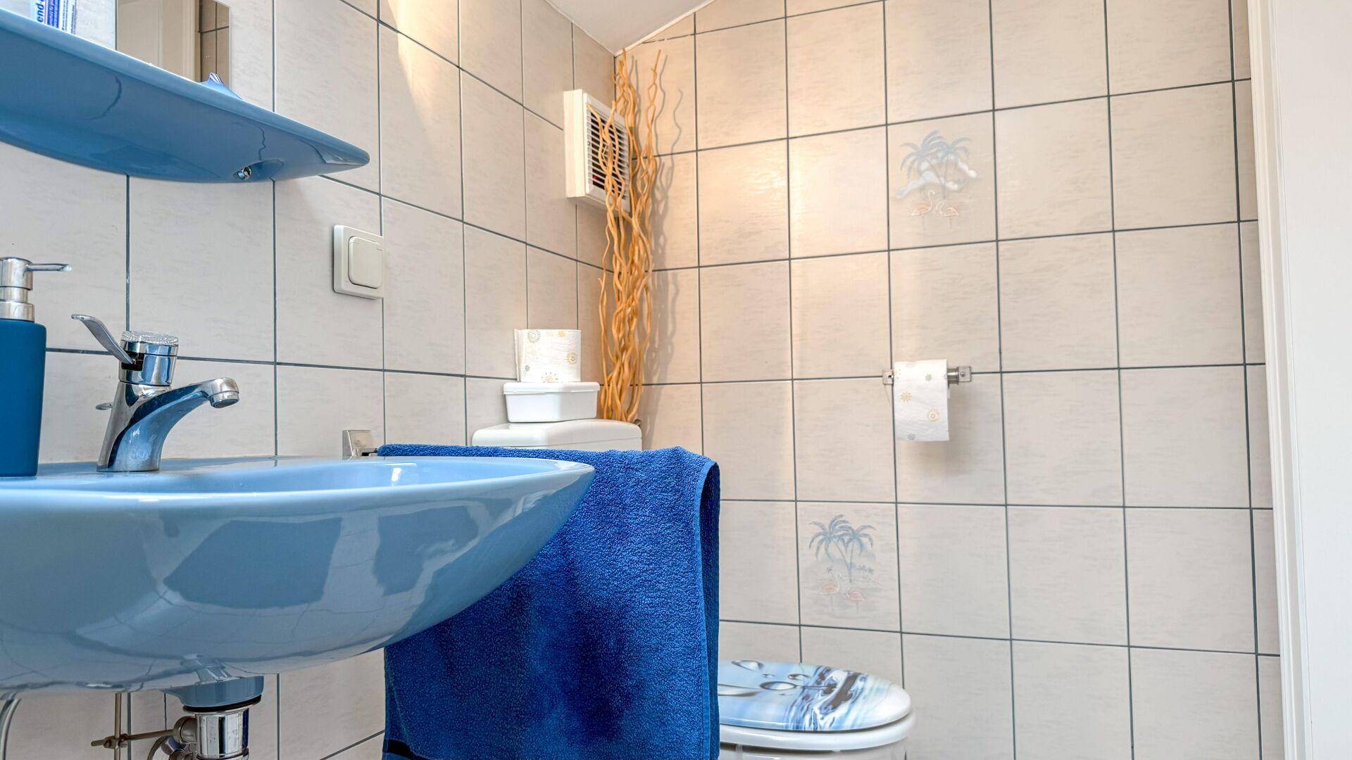 Kleines WC mit blauer Keramik, Fliesen und einem Fenster für Belüftung.
