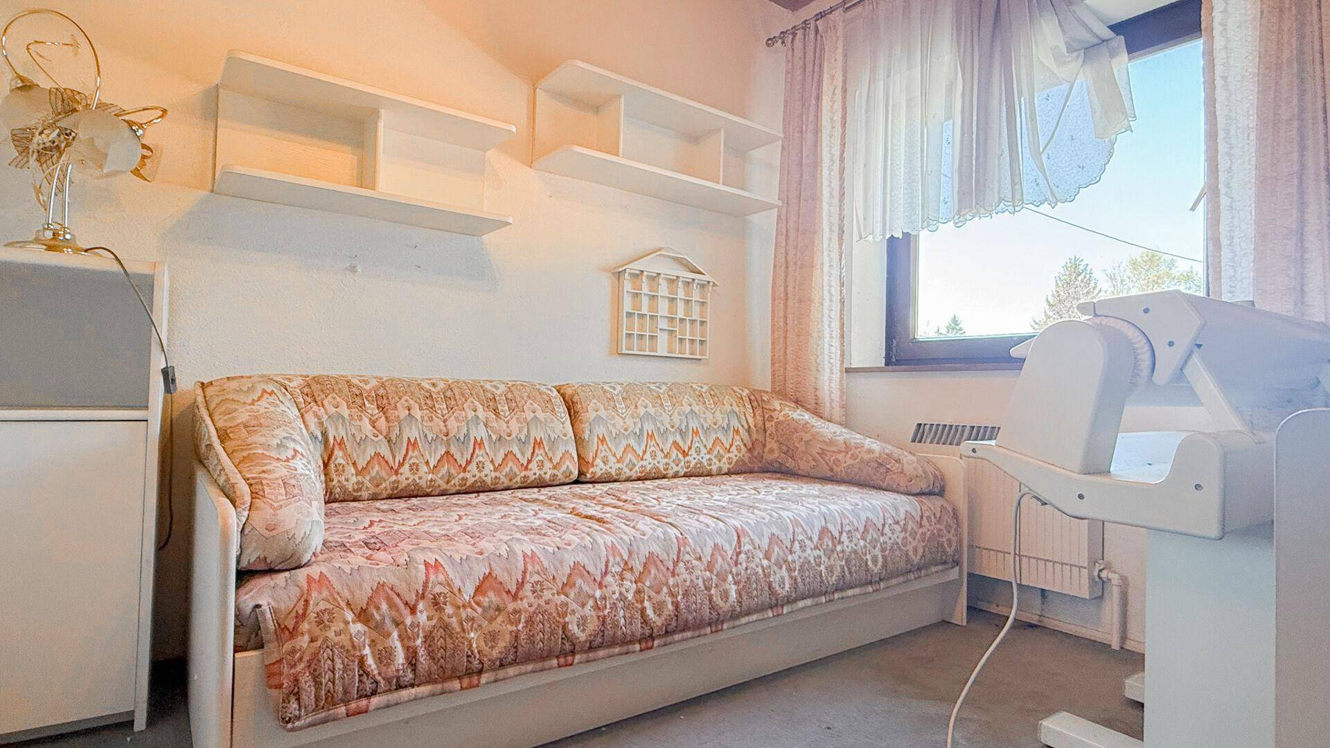 Helles Schlafzimmer mit Tagesbett und Wandregalen, gut belichtet durch ein Fenster.