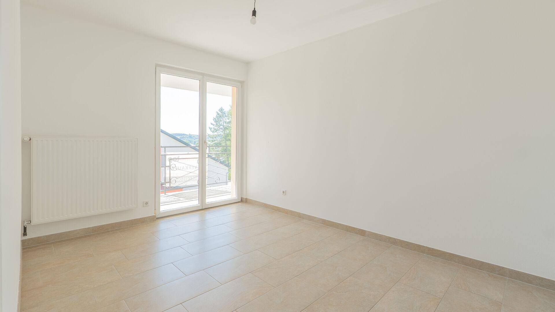 Heller Raum mit Fliesenboden und Zugang zu einem Balkon durch eine Glastür.