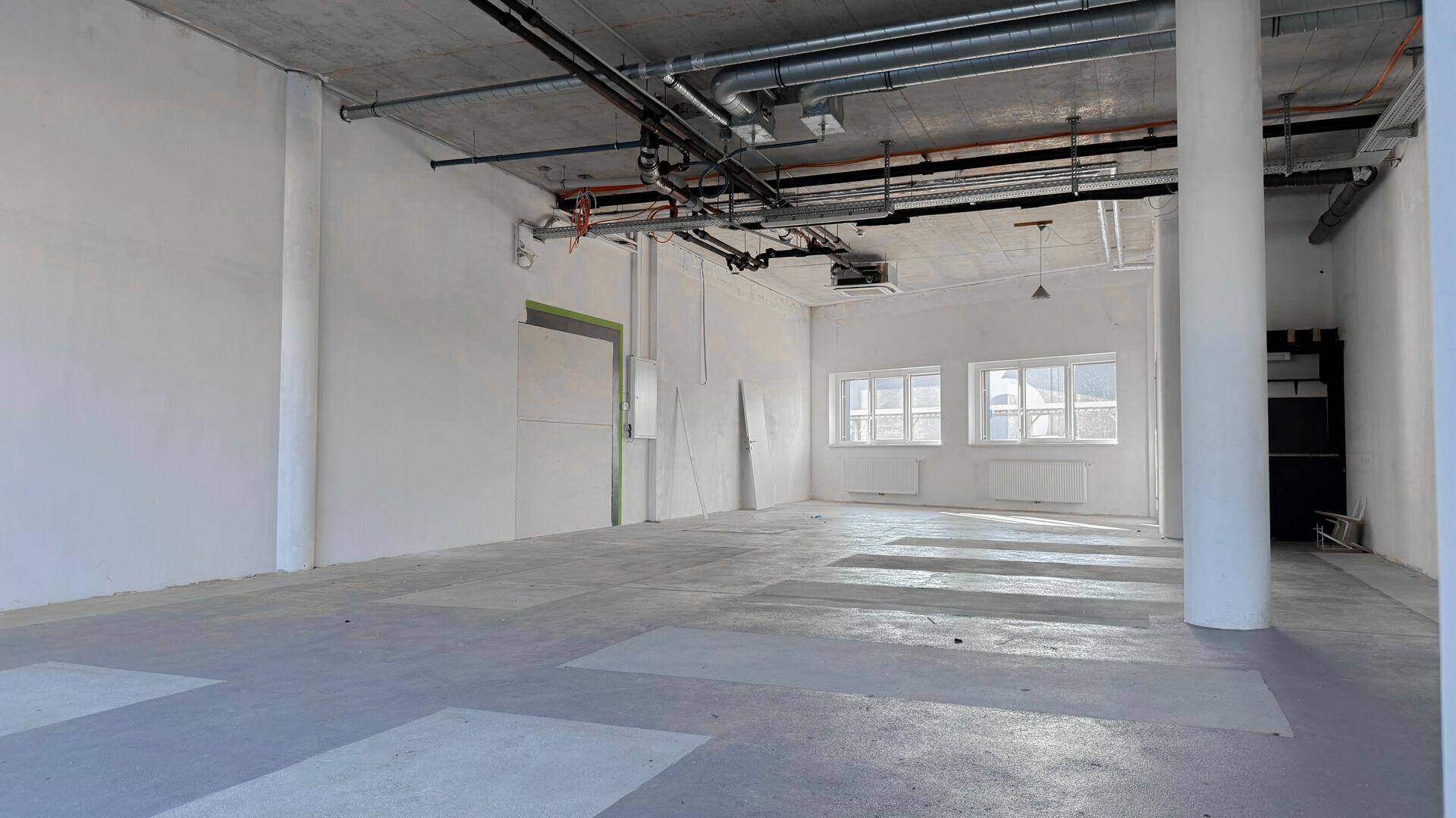 Heller, weitläufiger Innenraum mit Betonboden und sichtbaren Leitungen, ideal für gewerbliche Nutzung.